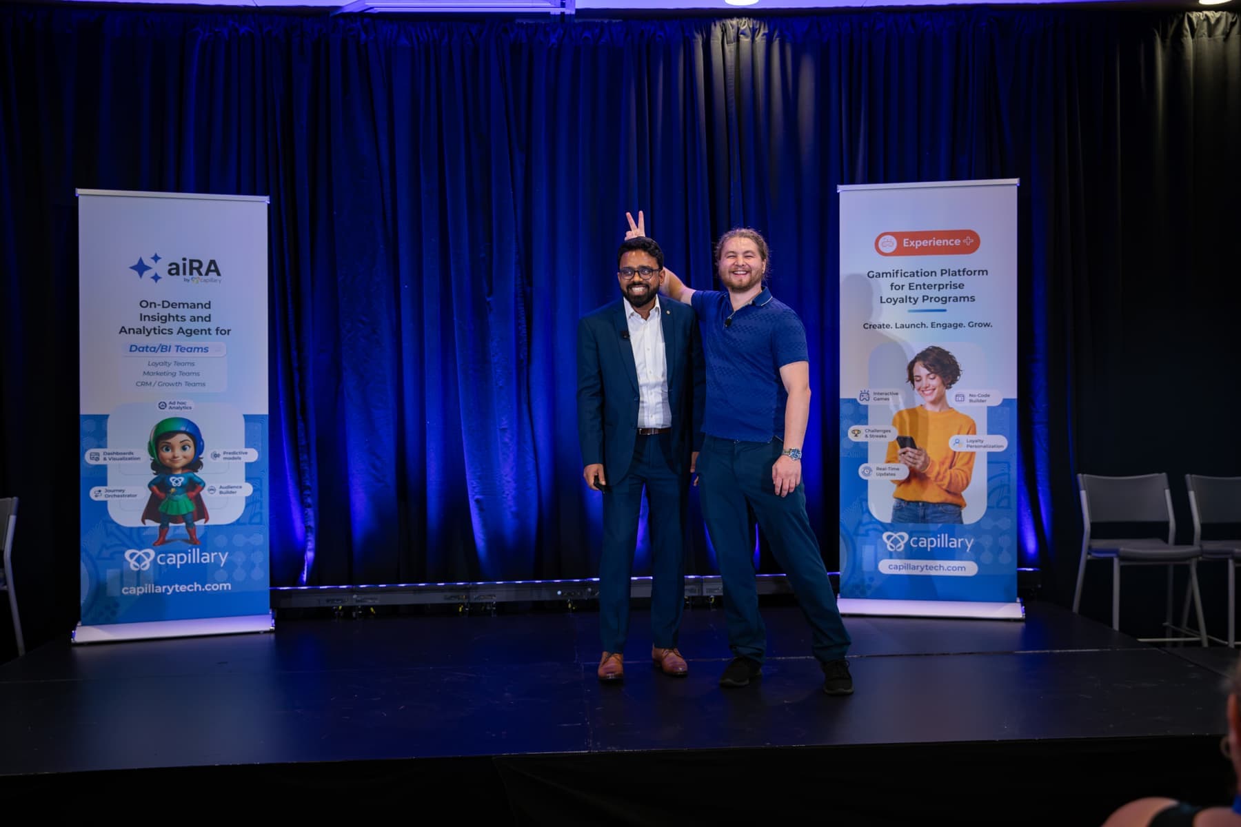 Two presenters on stage, one giving the other bunny ears