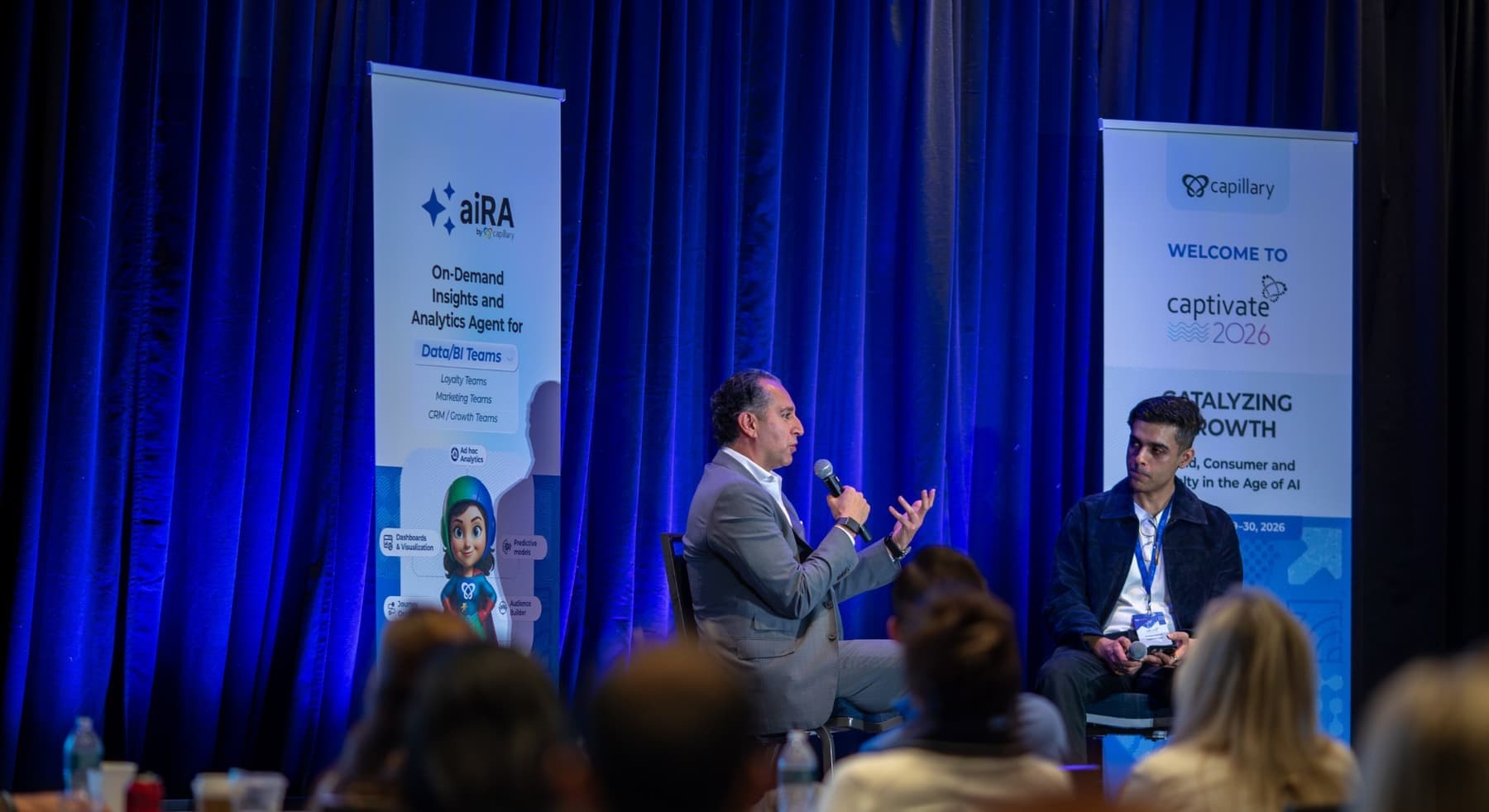 Two speakers in a fireside conversation on stage, with Captivate banners behind them