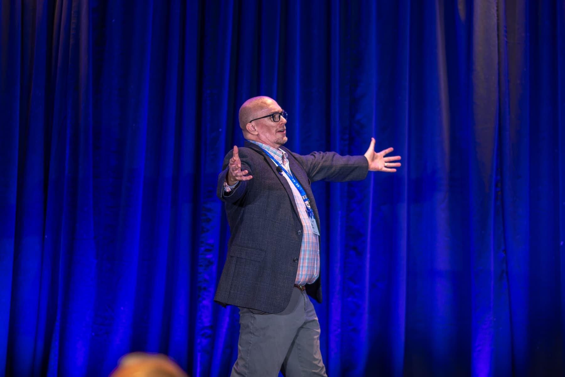 A speaker on stage with arms spread wide
