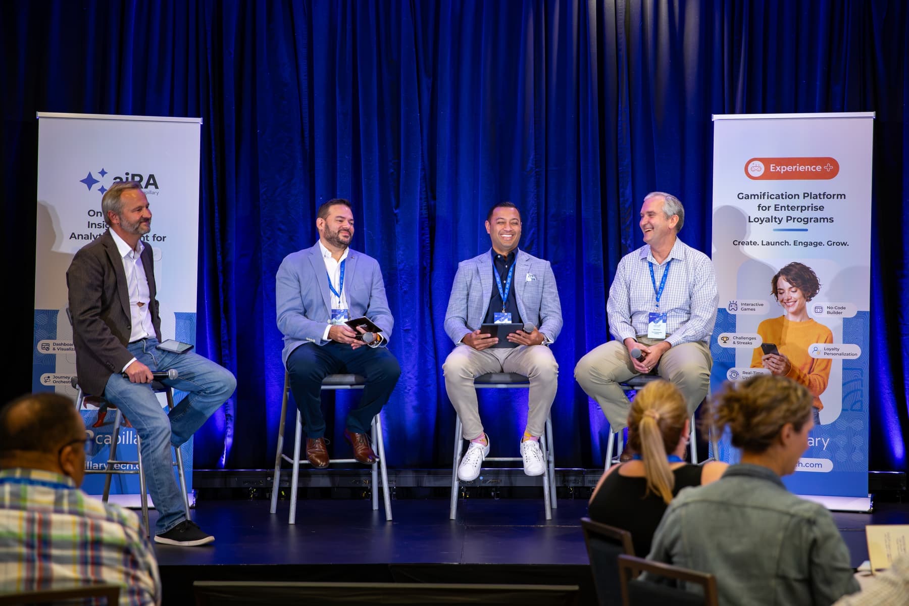 Four panelists laughing on stools on stage