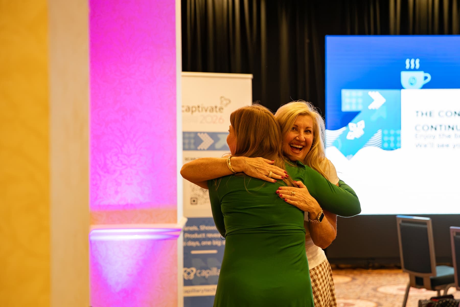 Two attendees hugging next to a pink-lit pillar
